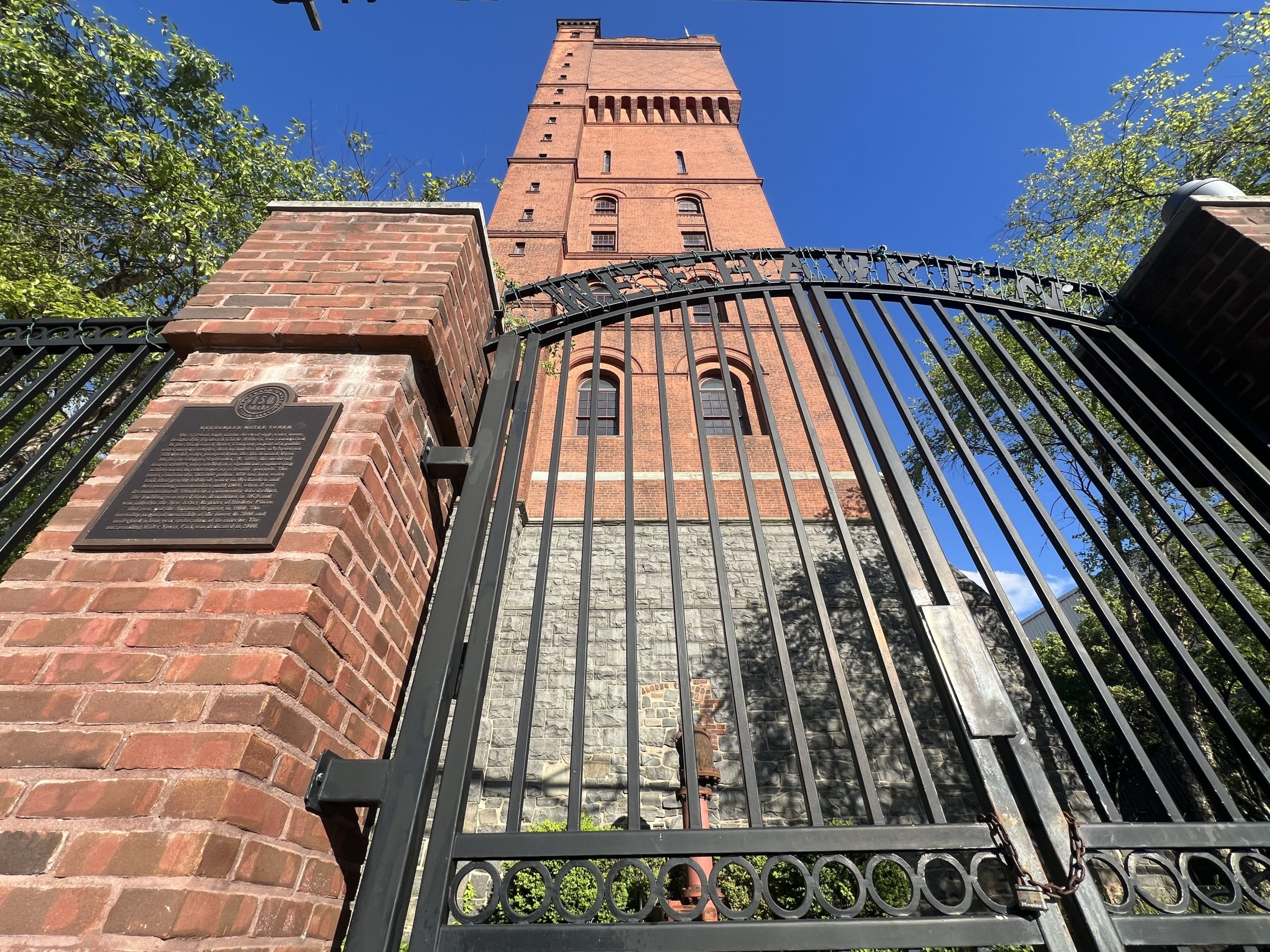 Gates that say Weehawken outside water tower with a bright blue sky beyond