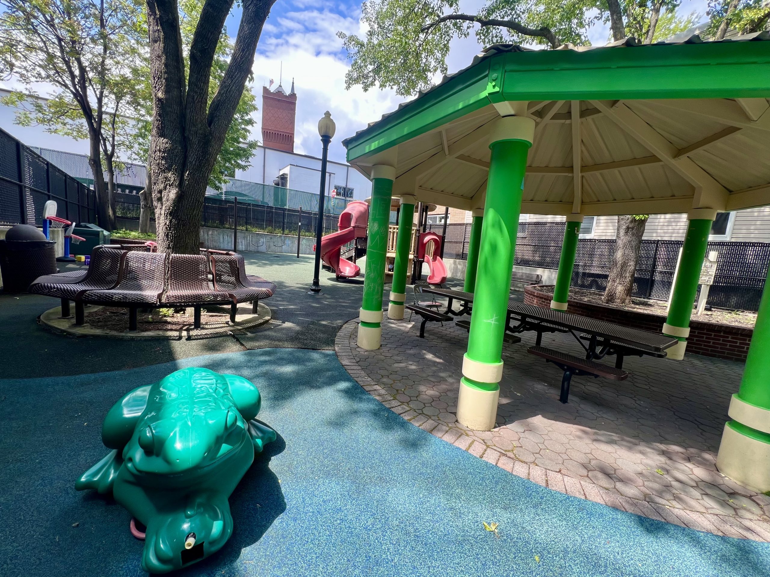 small park with frog sprinkler and playground with water tower in background